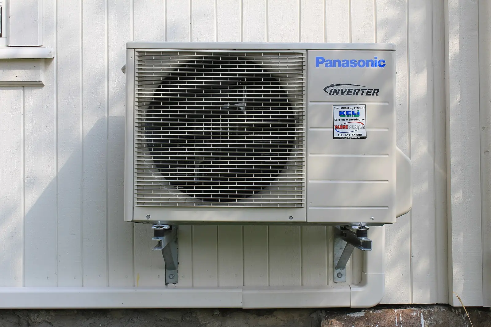 Inverter heat pump outdoor unit mounted on brackets on a house wall