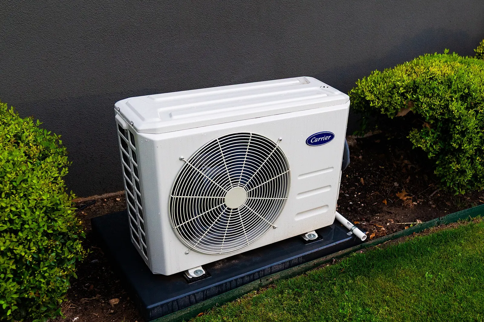 Outdoor central air and heat pump unit on a pad beside a house